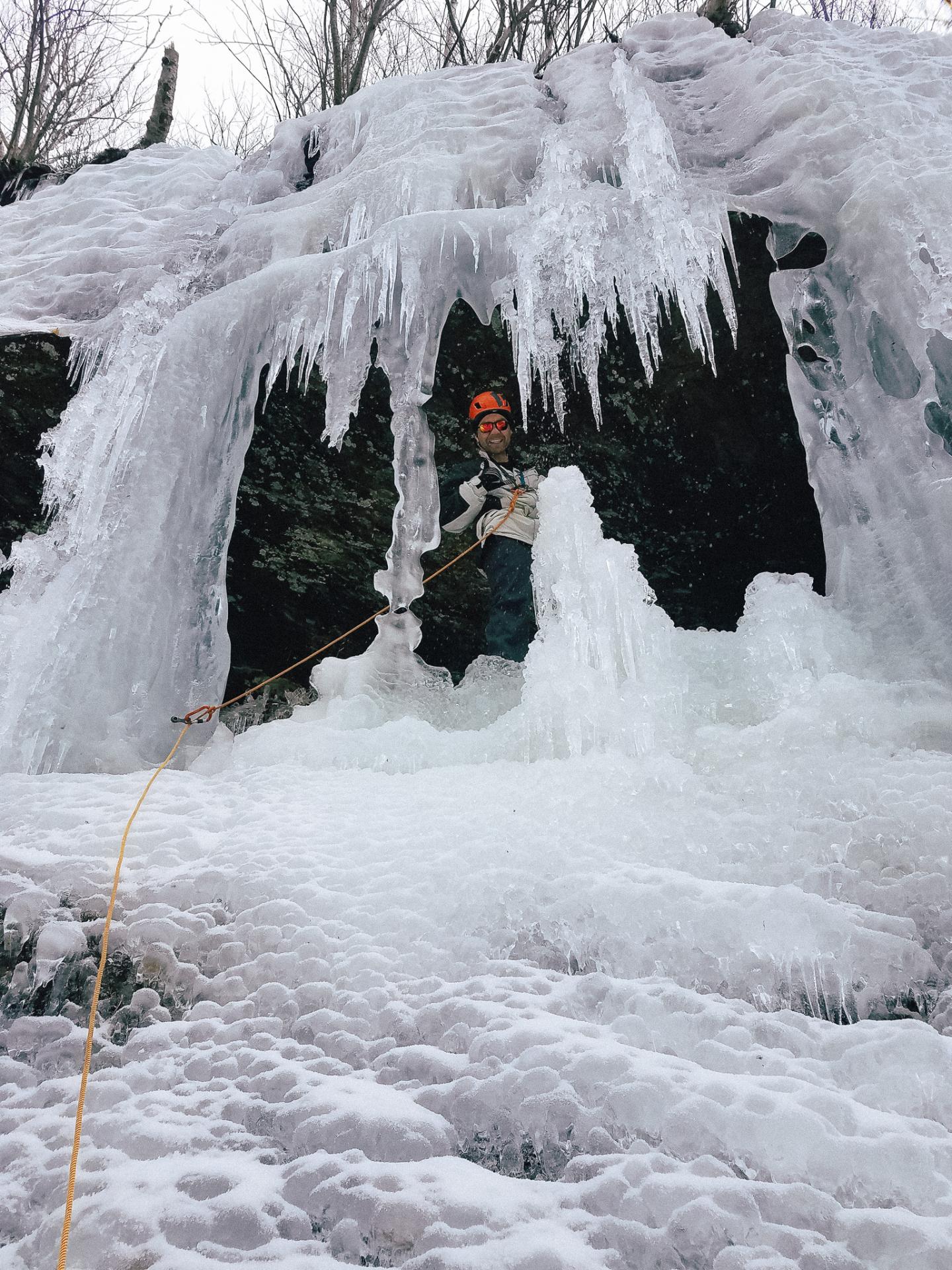 Climber with helmet scales icy formation, rope attached.