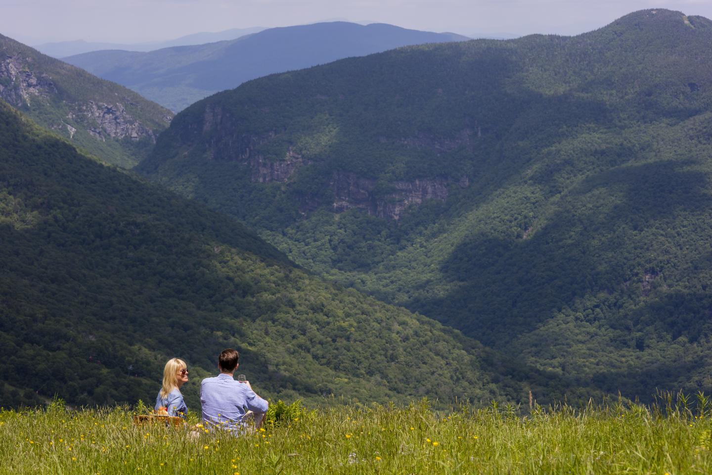 Couple sitting on grassy hill, admiring lush green mountains.