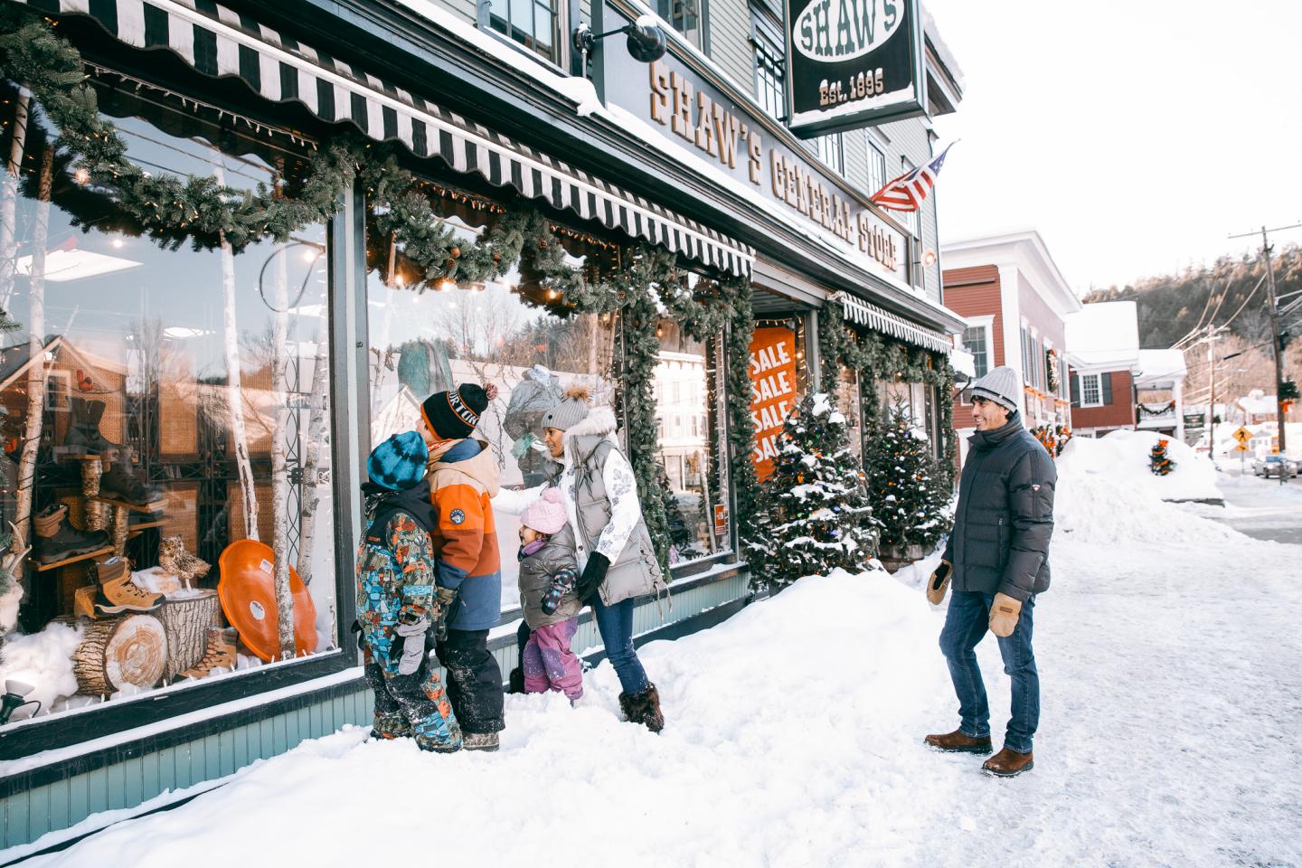 Family in winter clothing window shopping on a snowy street.
