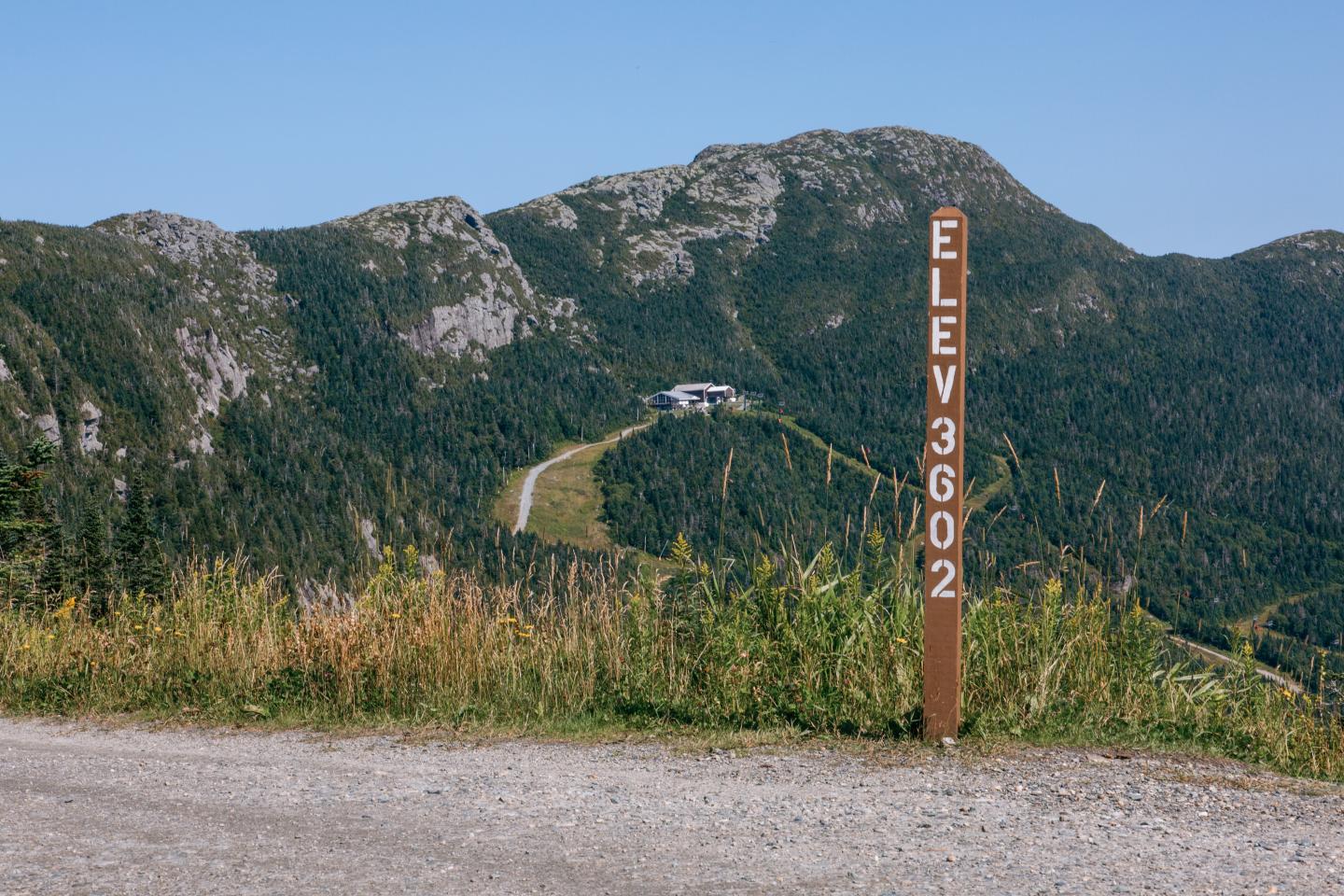 Mountain landscape with elevation sign, green hills, and clear blue sky.