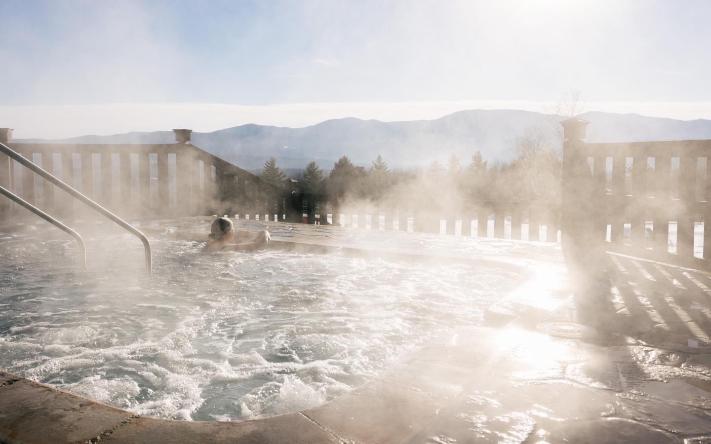 Steamy hot tub overlooking snowy mountains.