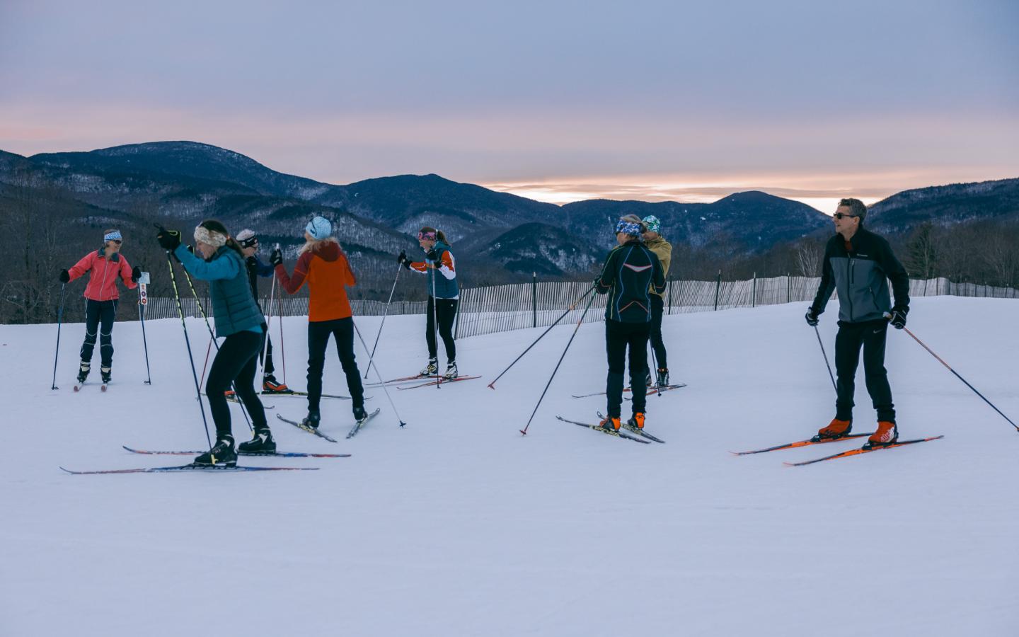 Cross-country skiers on a snowy trail, mountains in the background.
