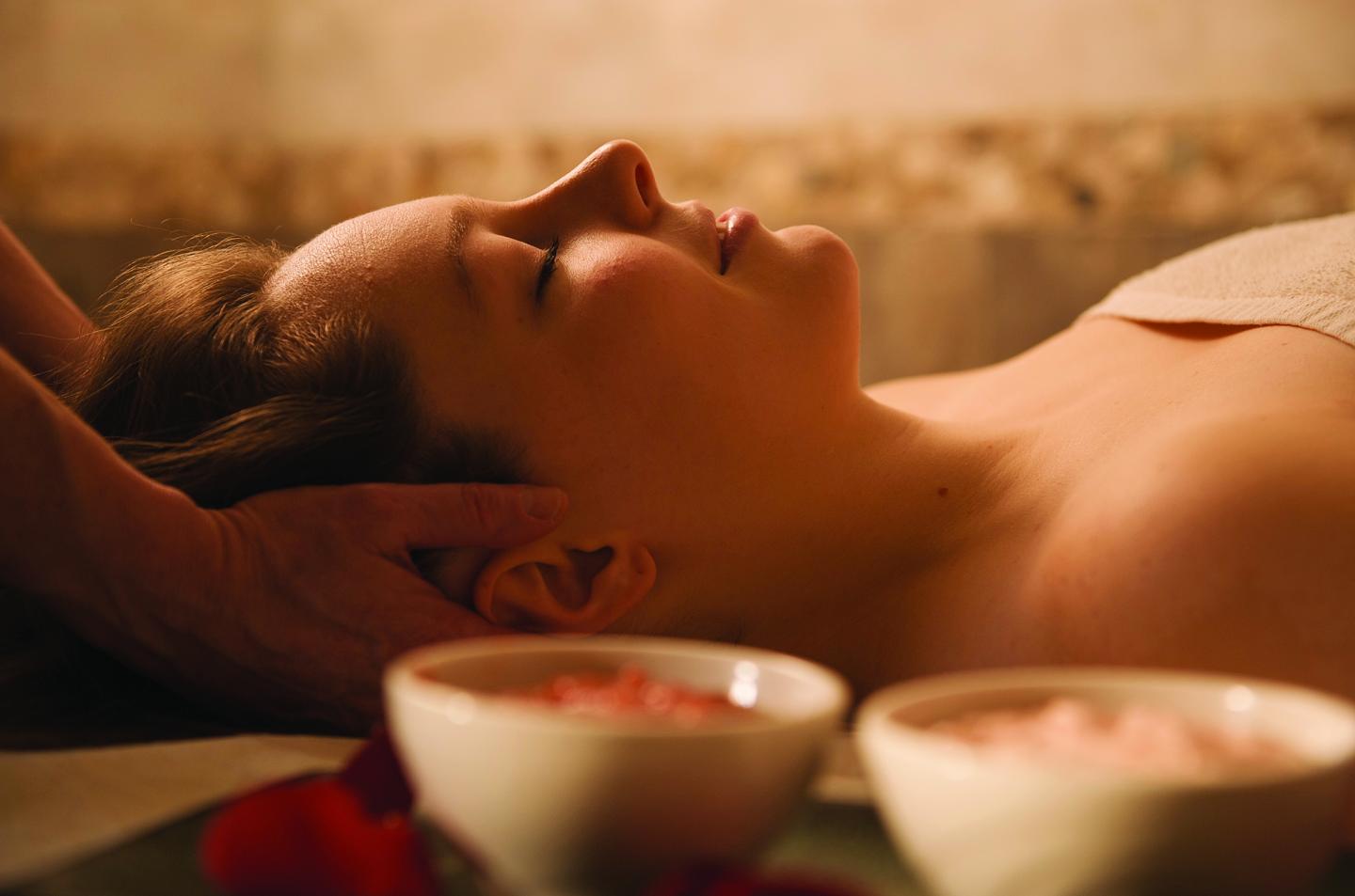 Person receiving a head massage with bowls of spa products nearby.