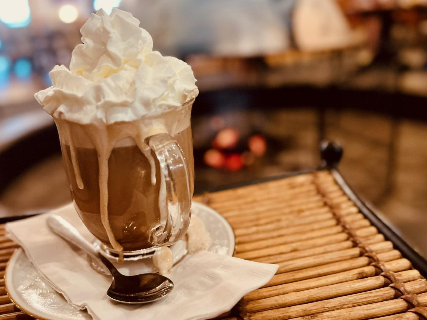 Hot chocolate with whipped cream on a table near a cozy fireplace.