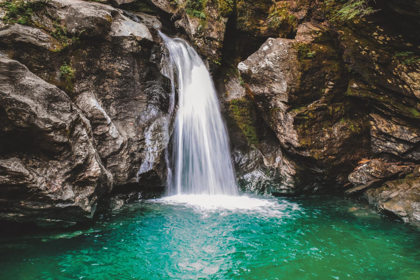 Waterfall cascading into a turquoise pool surrounded by rocky cliffs.