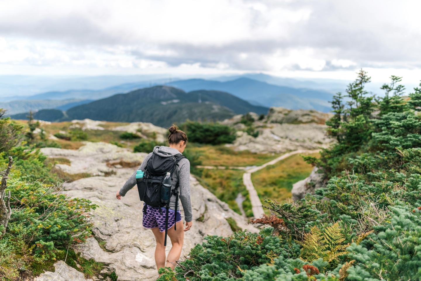 Hiker trekking rocky mountain path under cloudy sky.