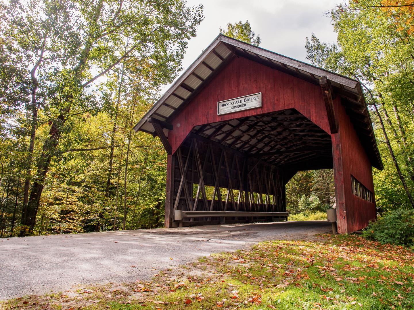 Red covered bridge in a wooded area during autumn.