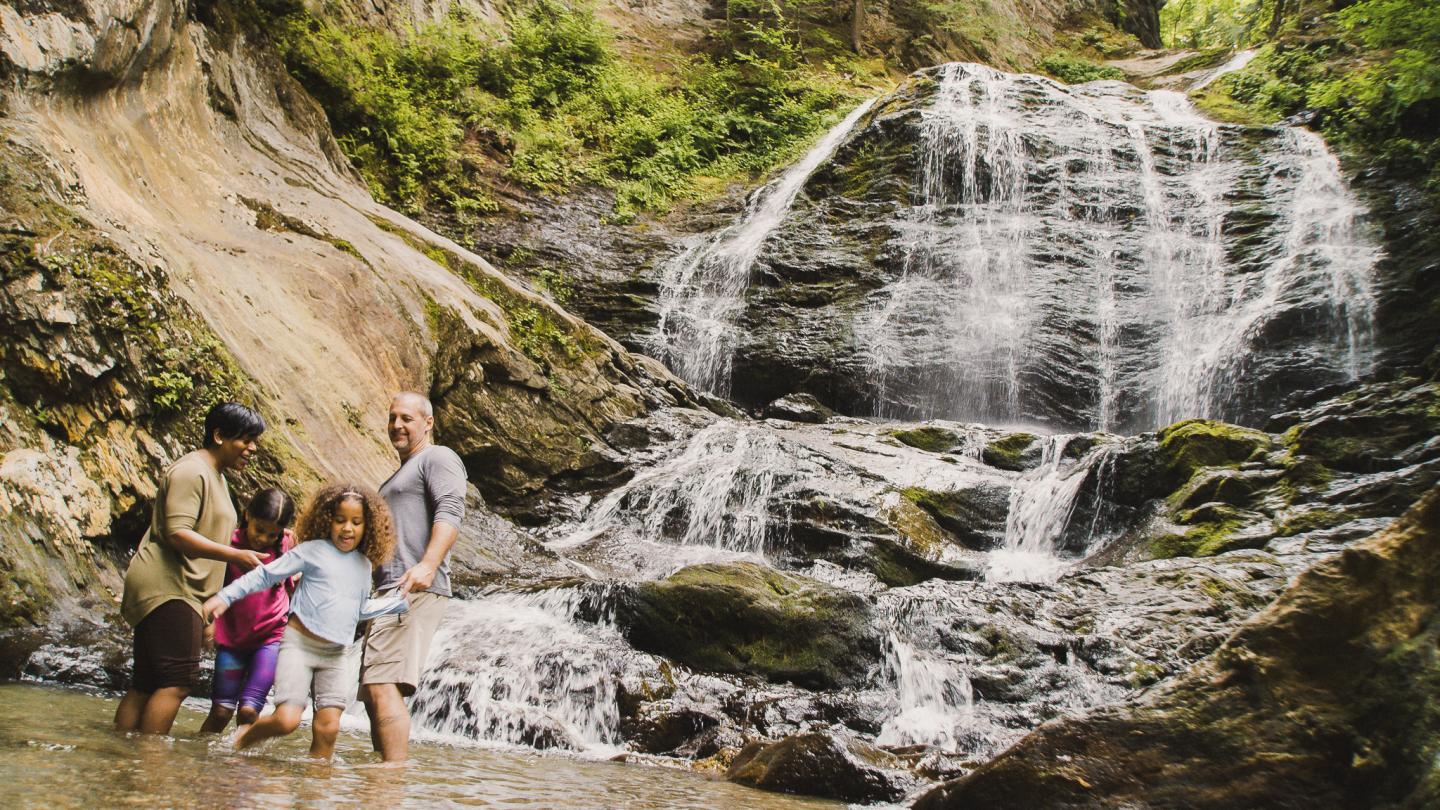 Family wading in shallow water near a cascading waterfall.