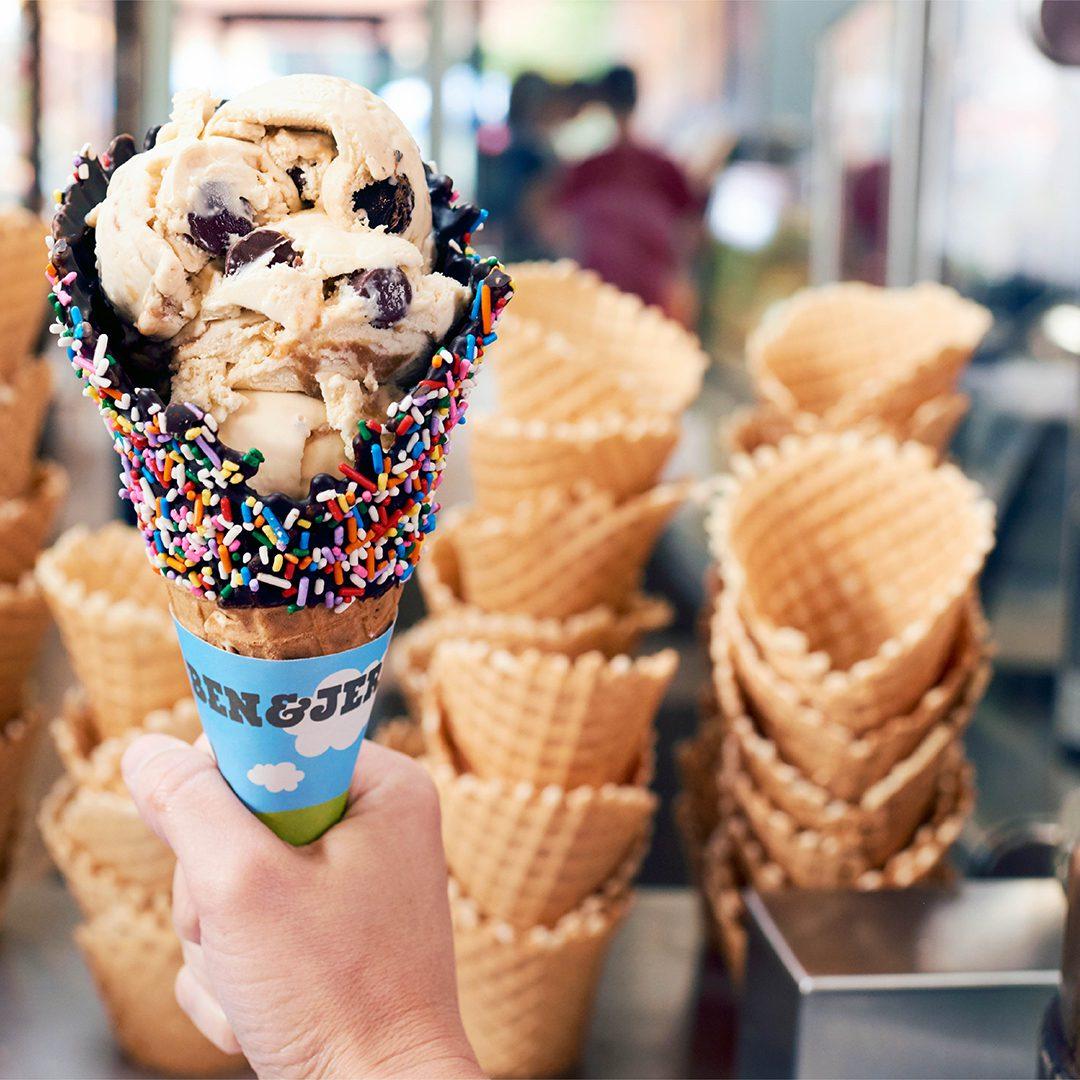 Ice cream cone with sprinkles held in front of waffle cones in store.