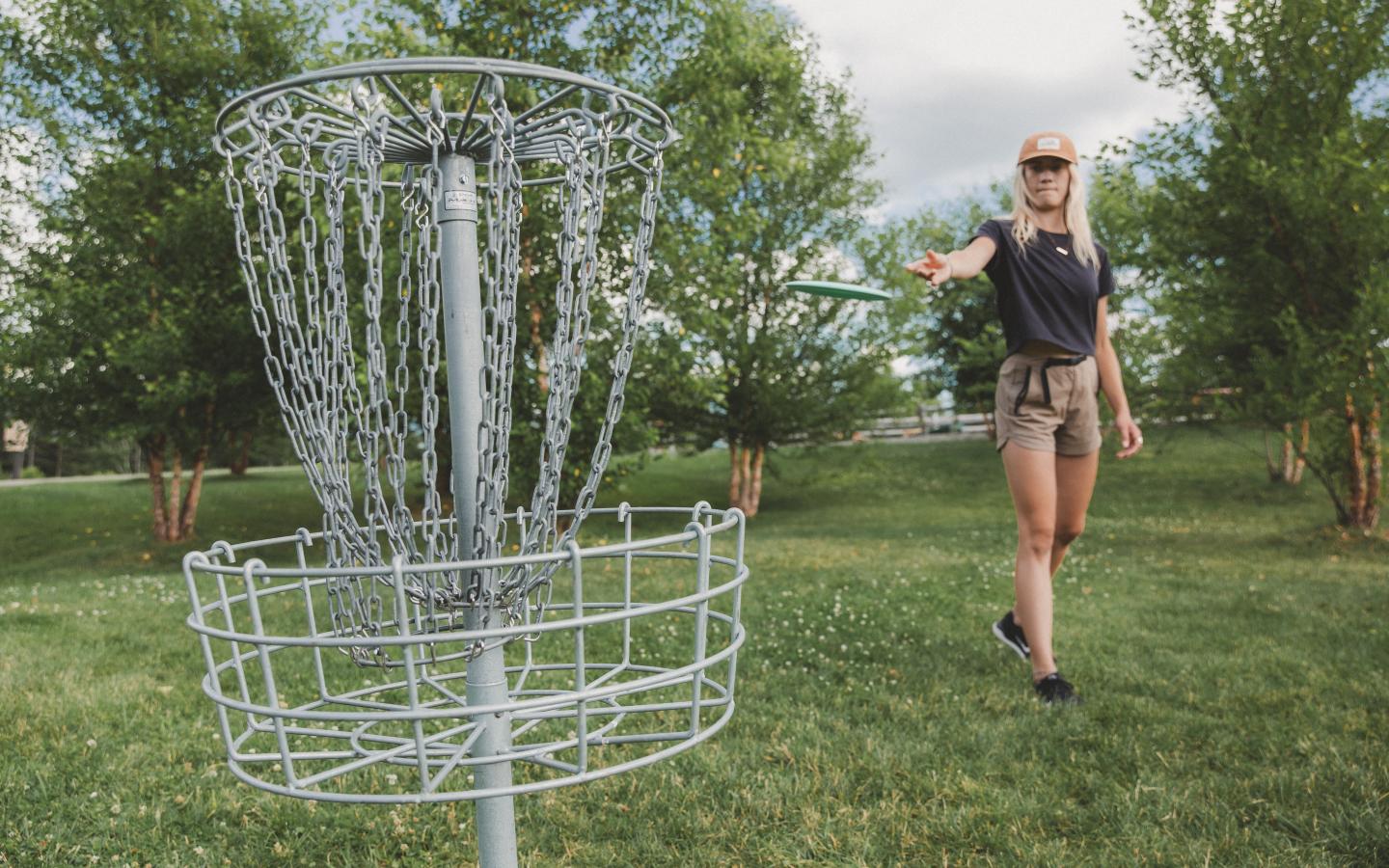 Person playing disc golf in a park, aiming for the metal basket.