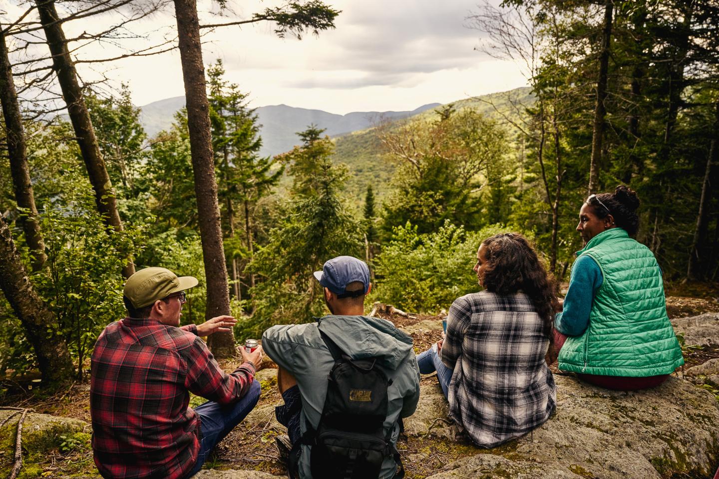 Four people sitting on a hill, overlooking a forest and mountain view.