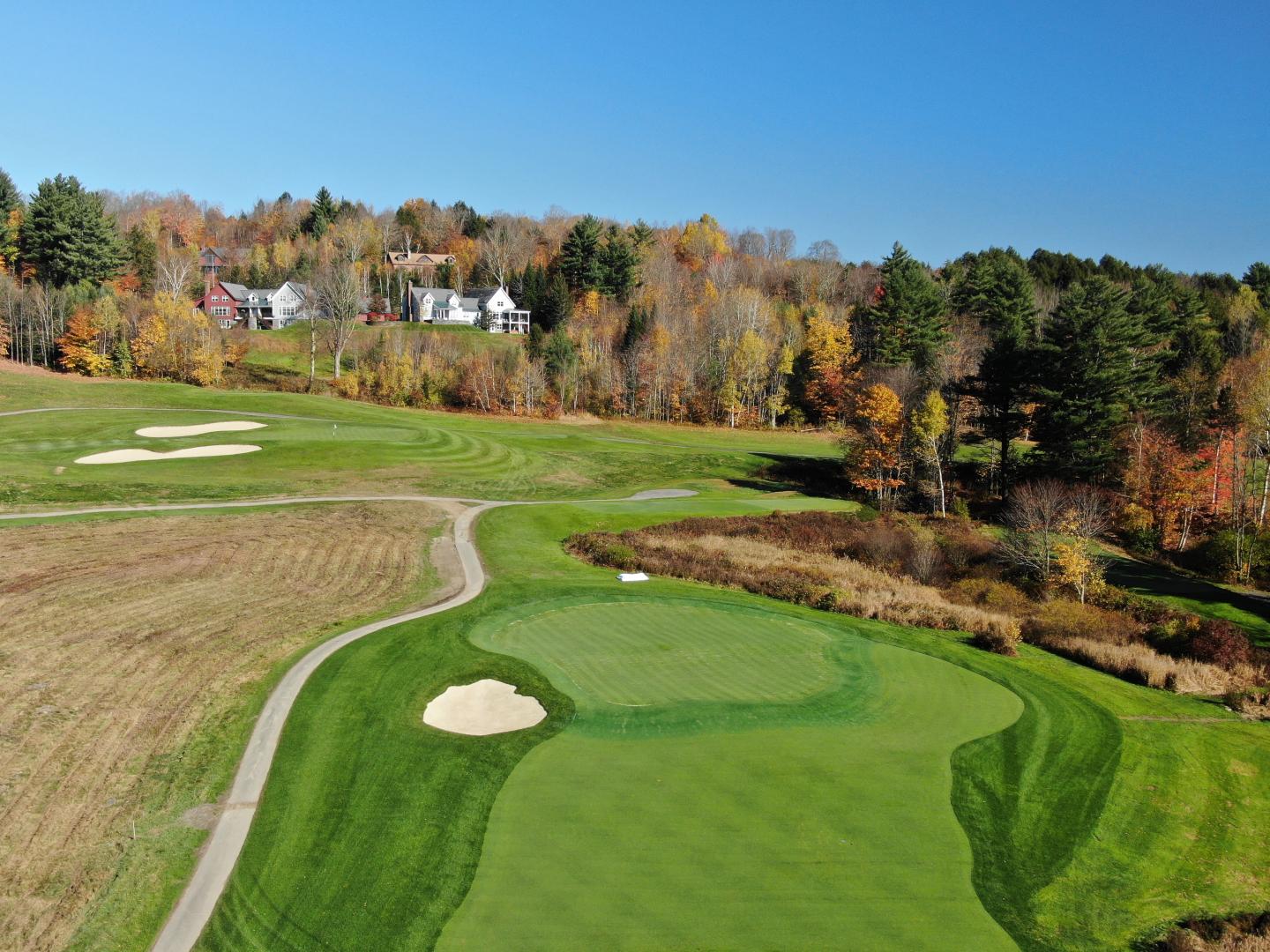 Golf course with sand traps, trees, and autumn foliage under a clear blue sky.