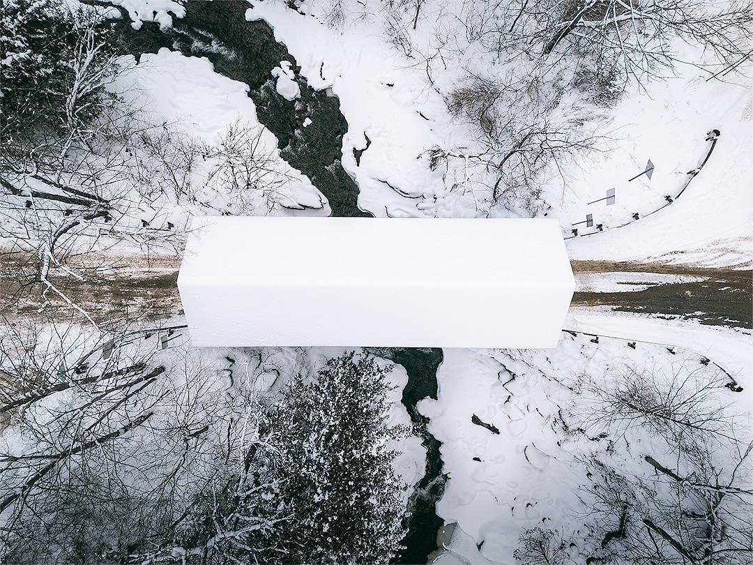 Snowy landscape with a white bridge over a winding creek.