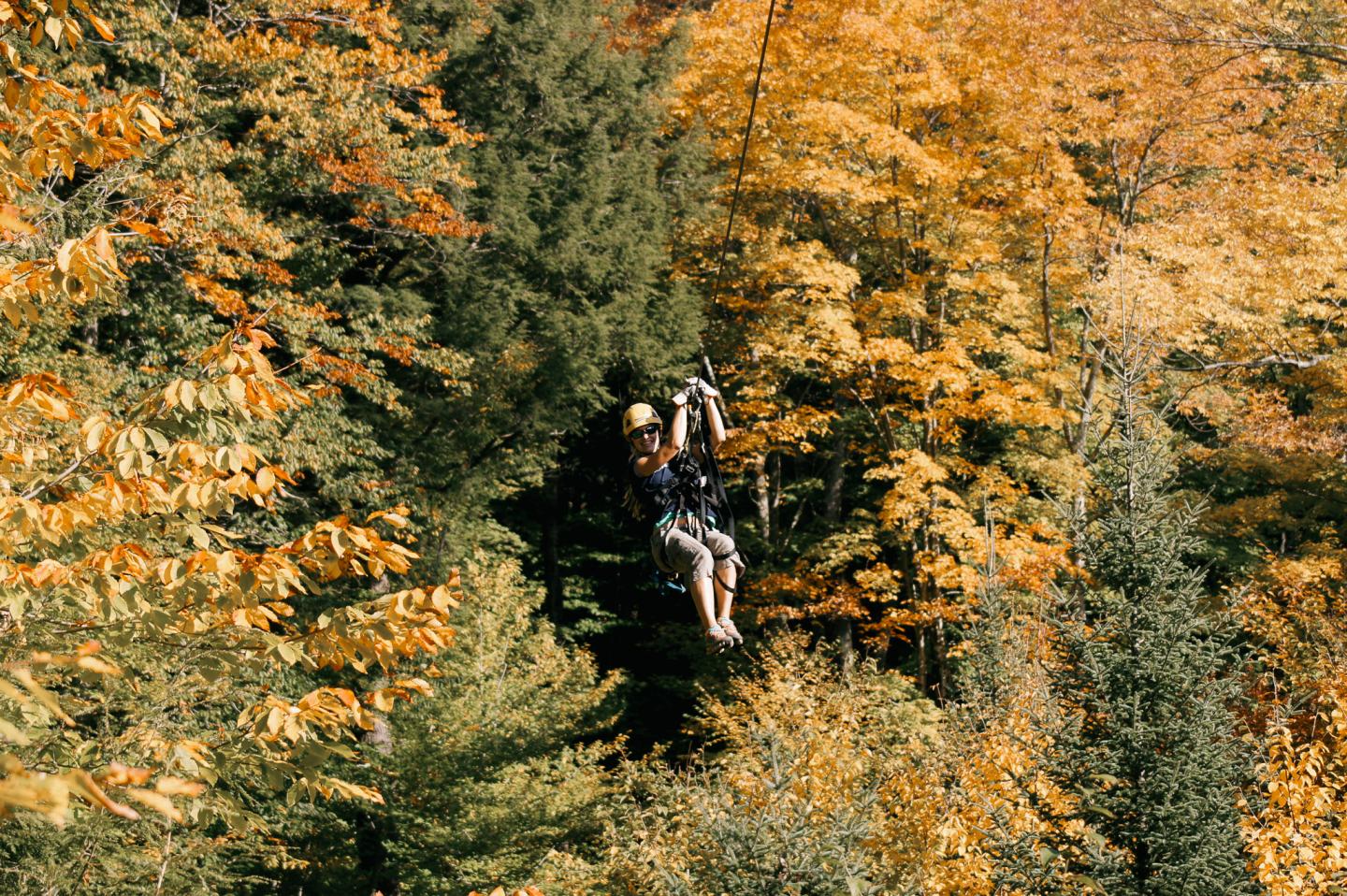 Person ziplining through colorful autumn trees.
