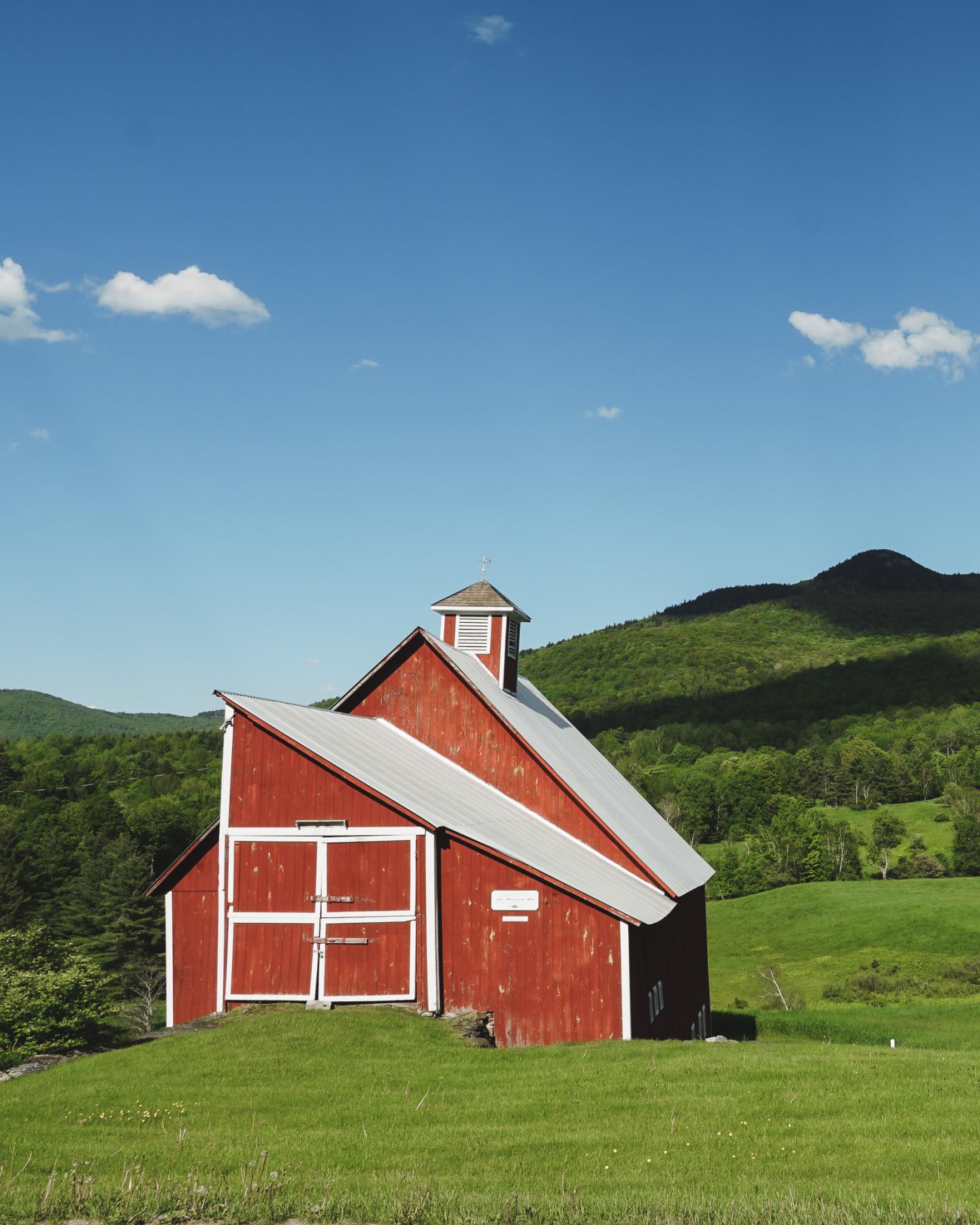 Red barn on a green hillside under a clear blue sky.