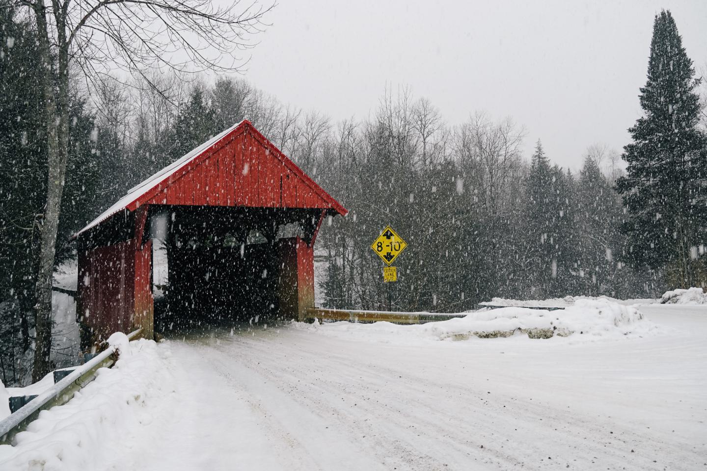 Red covered bridge in snowy winter landscape.