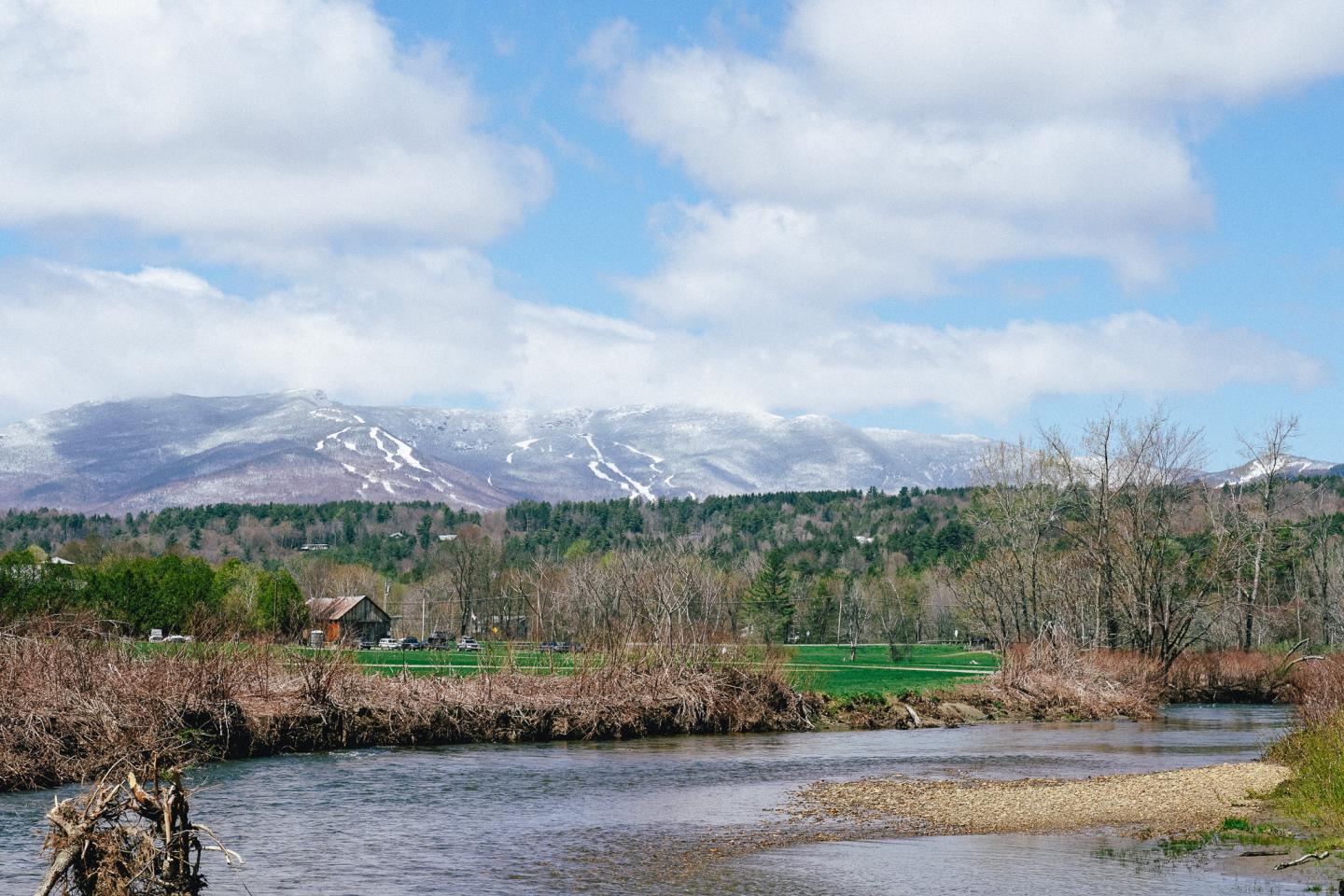 River with grassy banks, mountains, and cloudy sky in the background.
