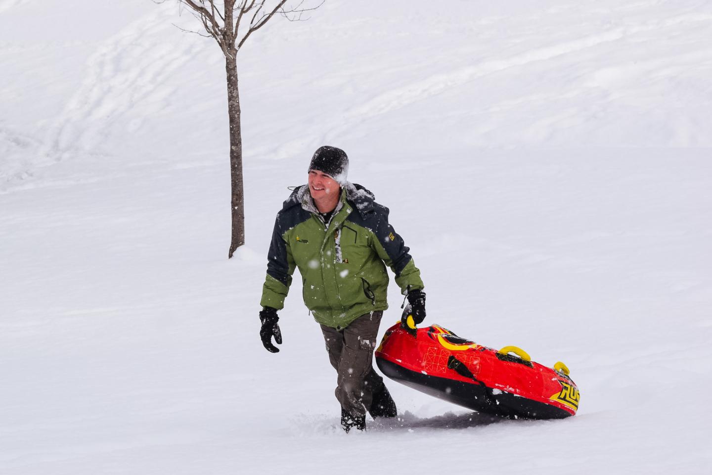 Man pulling red sled through snowy landscape.