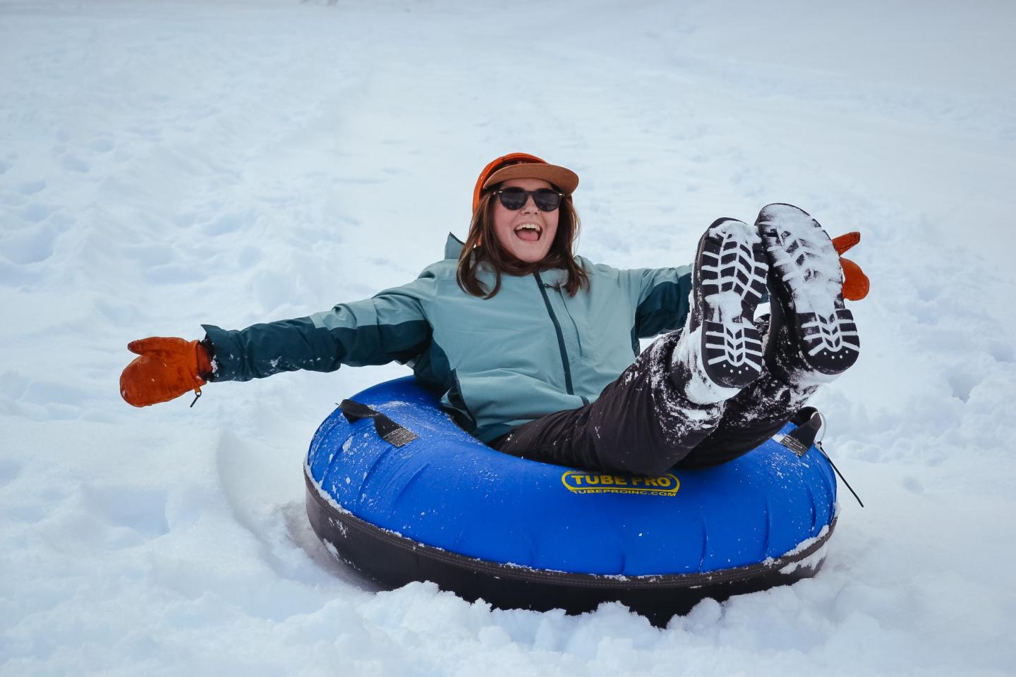 Person joyfully snow tubing in a blue inflatable, wearing winter gear.