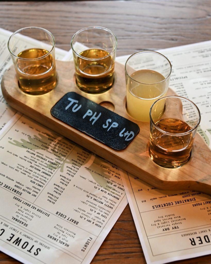 Four tasting glasses on a wooden flight board, menus underneath.