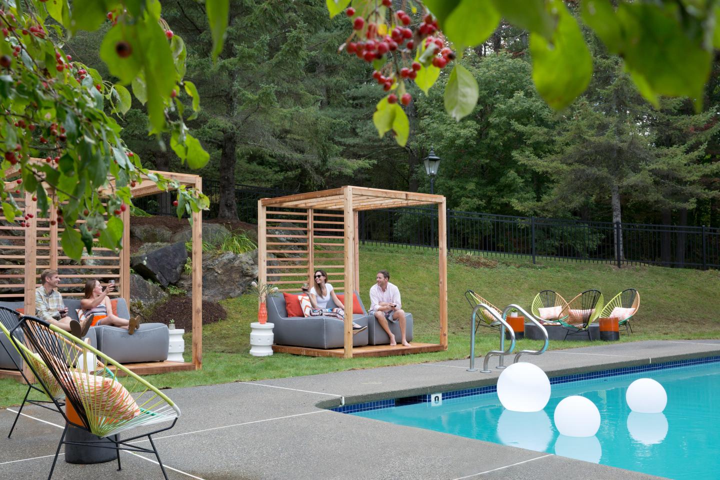Poolside with wooden cabanas and glowing spheres amid trees and greenery.