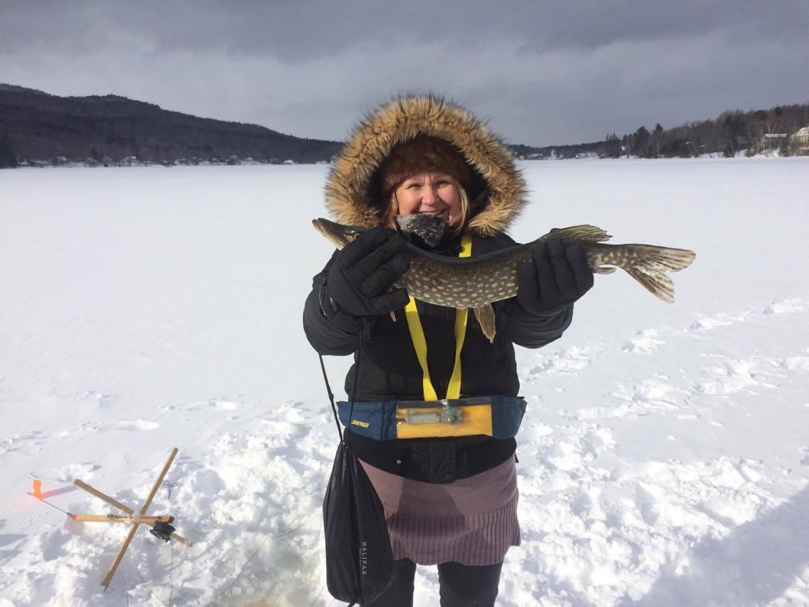 Person wearing a hooded coat holds a fish on a snowy landscape.
