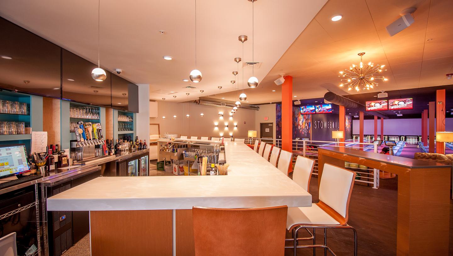 Modern bar with white counter, chairs, and hanging lights in warm tones.