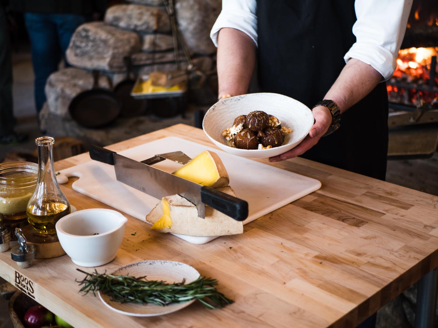 Chef holding a dish with meatballs over pasta, next to cheese on a cutting board.