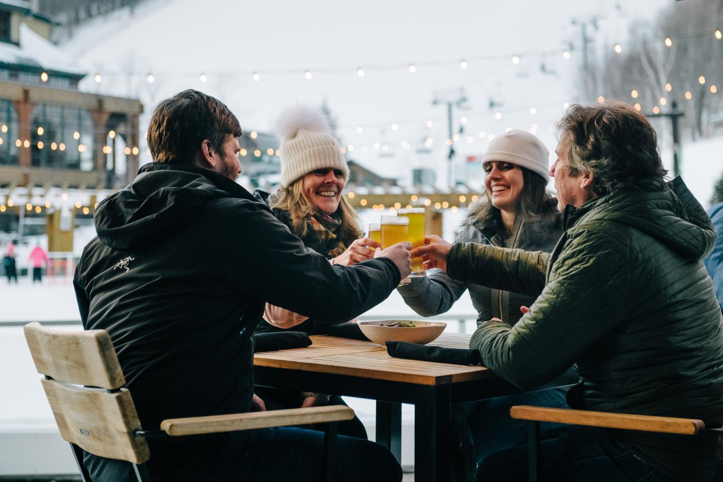 Group of friends toasting drinks at a snowy outdoor cafe.