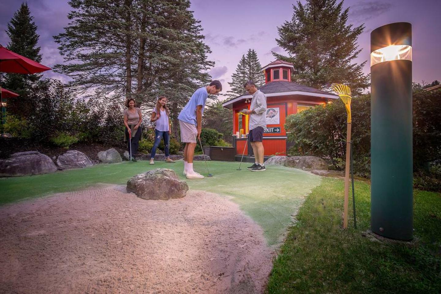 Mini-golf game at twilight, people playing near a lit pavilion.
