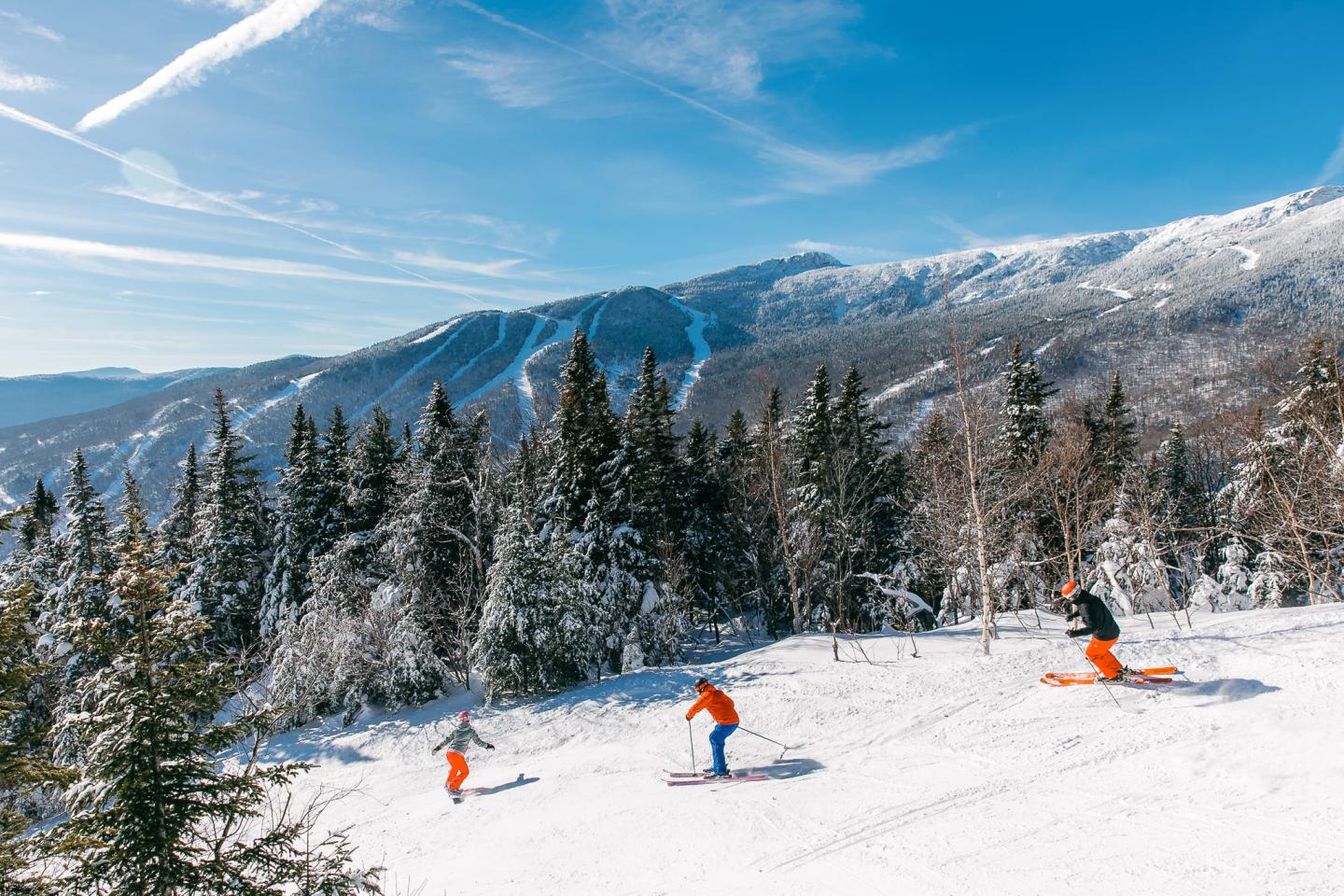 Skiers enjoying a run down a snowy mountain, clear blue sky above.