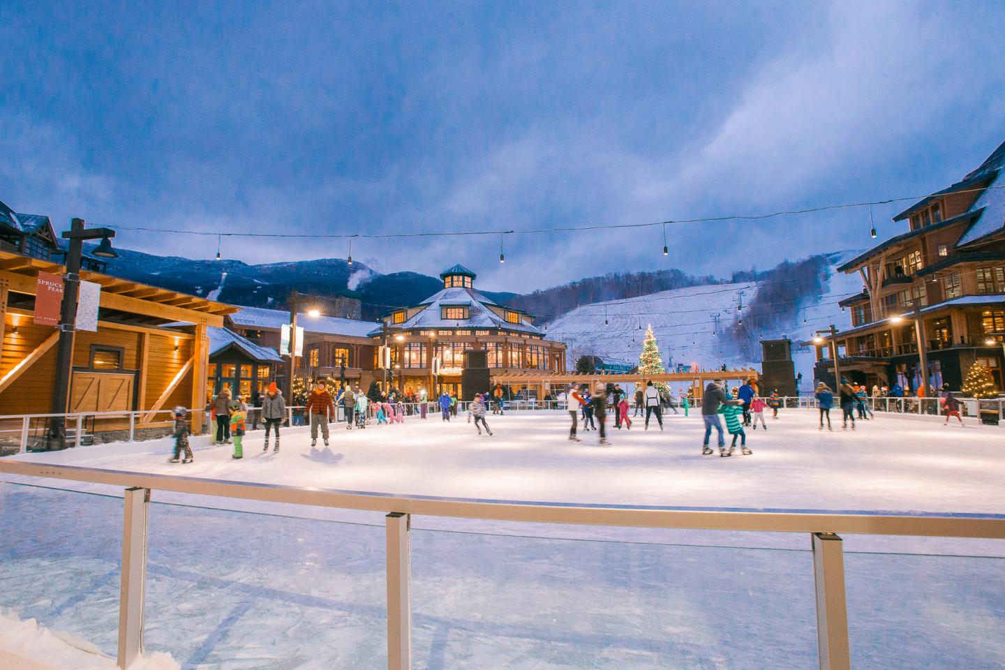 People ice skating in a festive village setting at dusk.