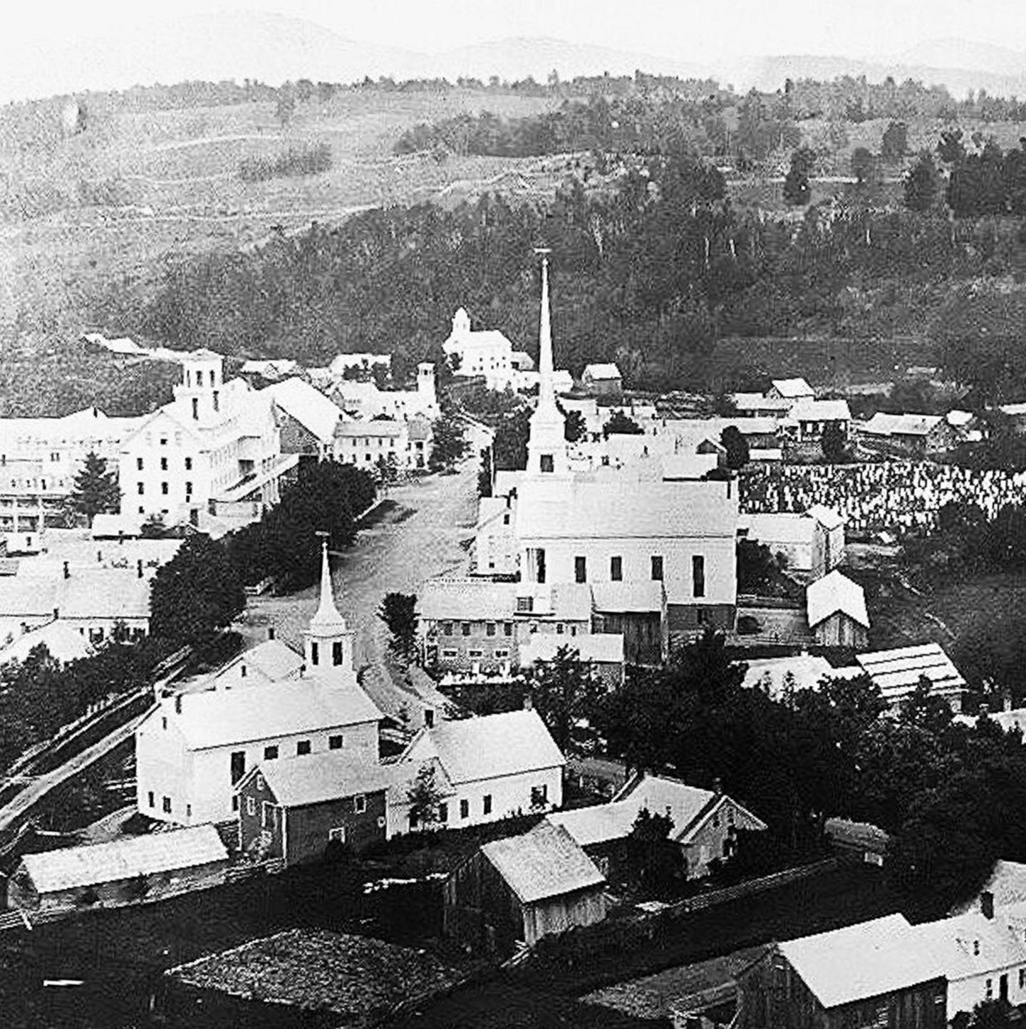 Historic town with churches, roads, and hills in the background, black and white photo.
