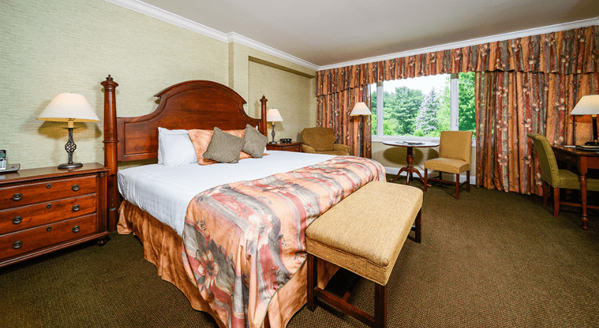 Elegant hotel room with a large bed, wooden furniture, and a view from the window.