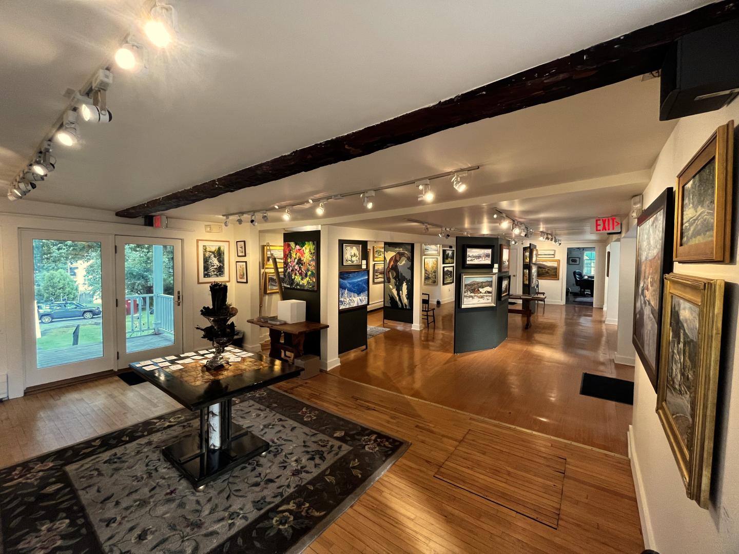 Art gallery interior with paintings on walls, lit by track lighting.