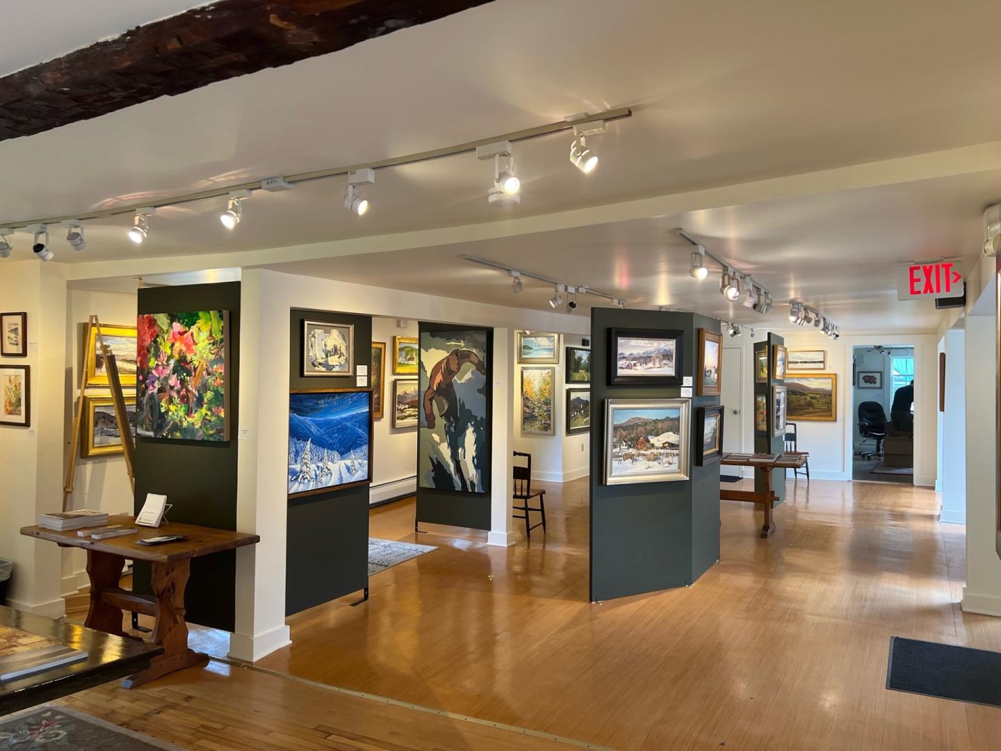 Art gallery interior with paintings on display, wooden floor, and soft lighting.