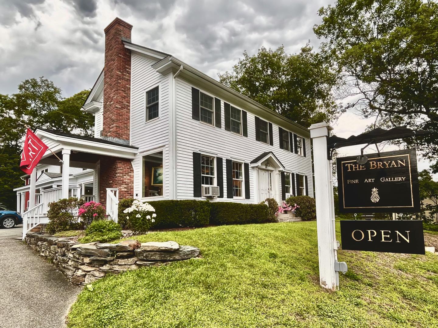 White two-story house with a red chimney and an "Open" sign in the front yard.