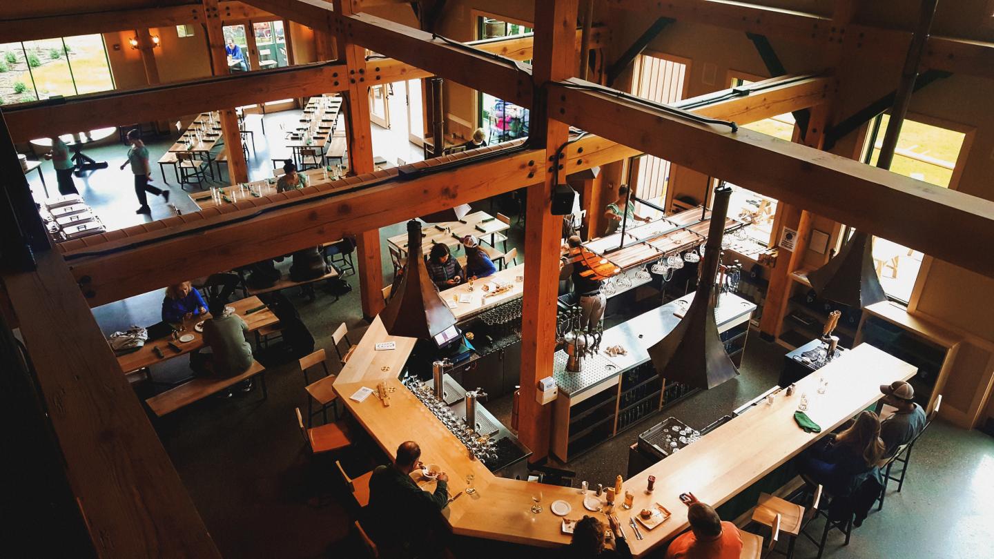Large, cozy cafe with wooden beams, people sitting at tables and bar.