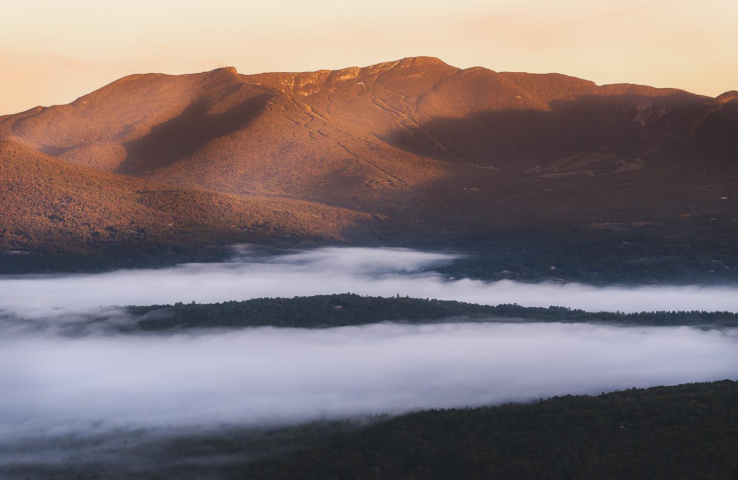 Mountain landscape at sunrise with low clouds and warm light.
