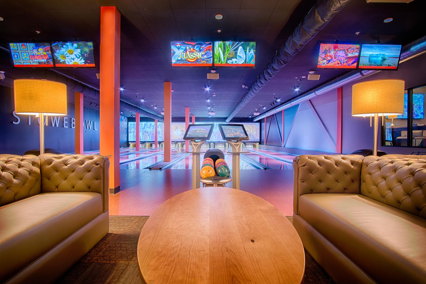 Bowling alley with colorful lanes, couches, and screens above.