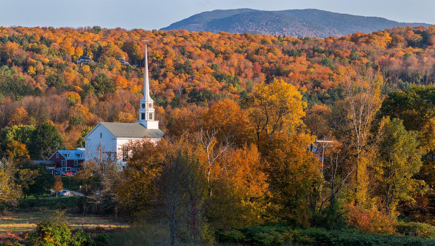 Church surrounded by vibrant autumn trees with mountains in the background.
