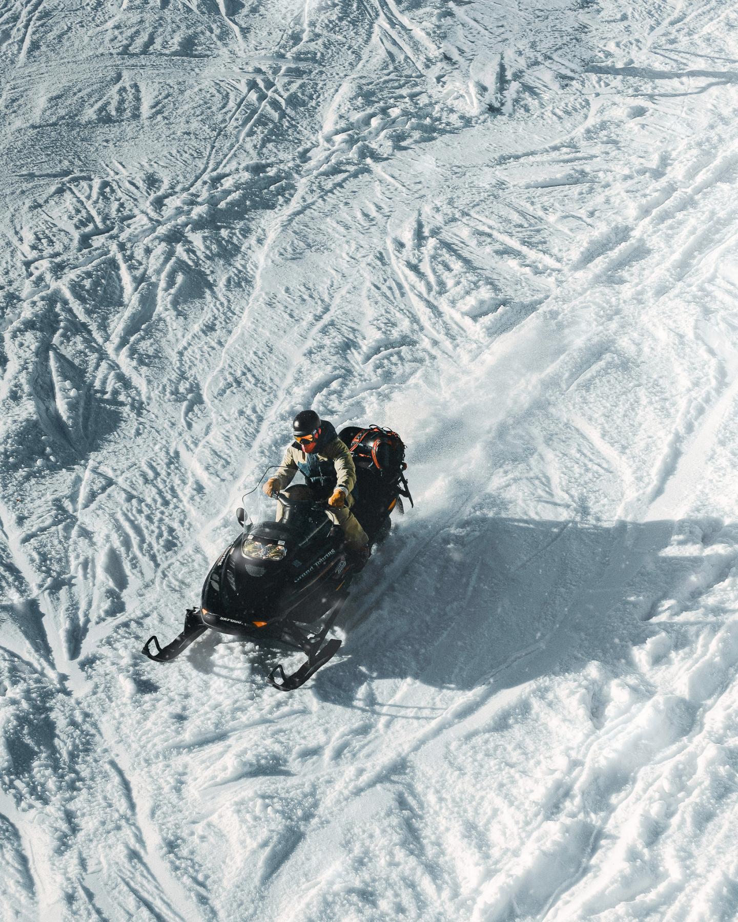 Snowmobile on snowy hill, two riders, bright sunlight.