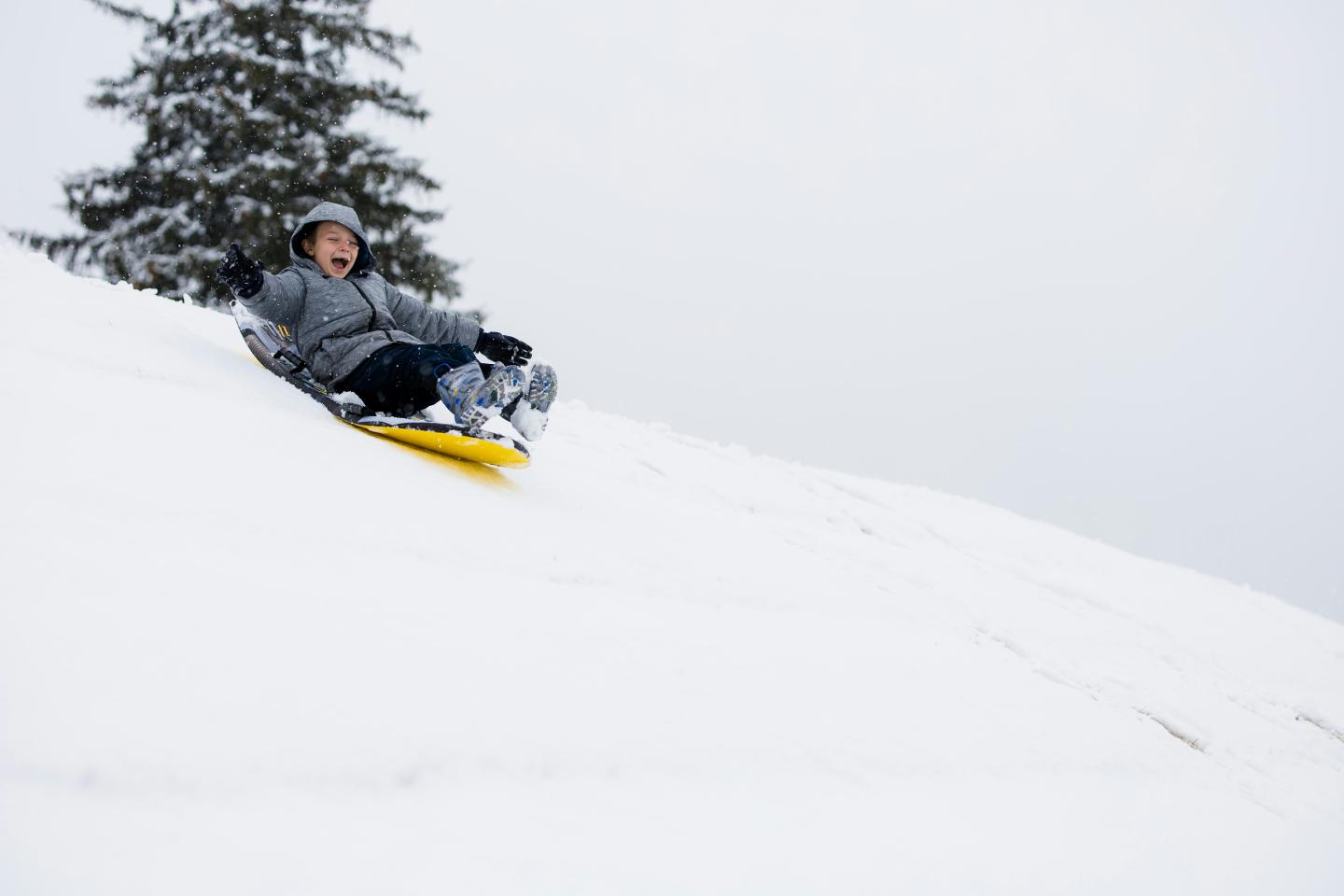Person sledding down a snowy hill, smiling in winter clothing.