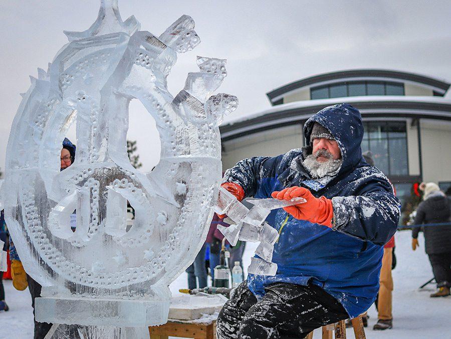 Man carving a detailed ice sculpture outdoors in winter.