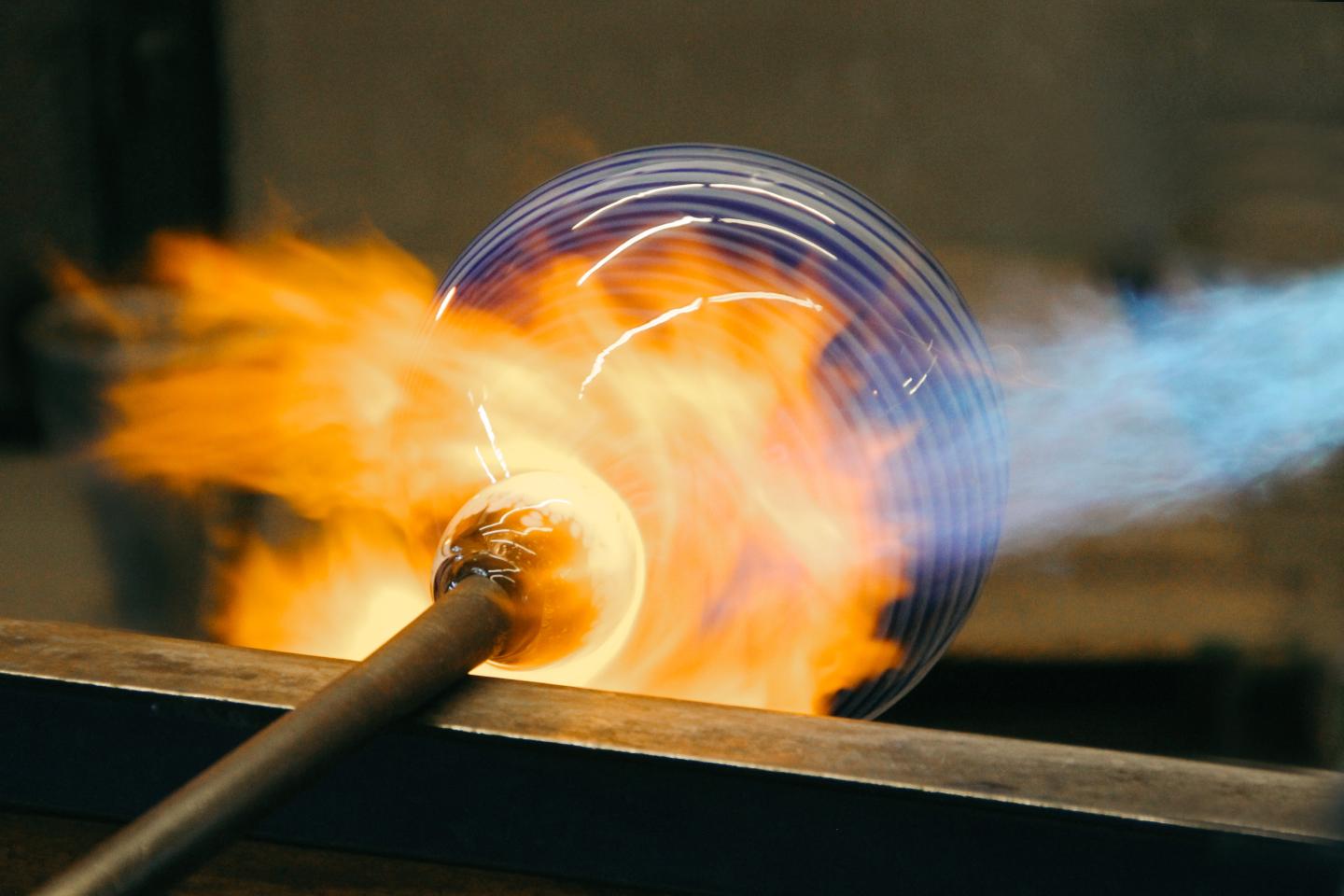 Glass being blown in a hot flame, glowing with orange and blue hues.