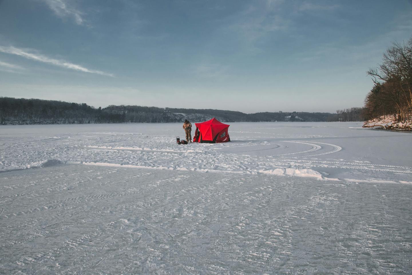 Frozen lake with red ice fishing tent and trees in the distance.