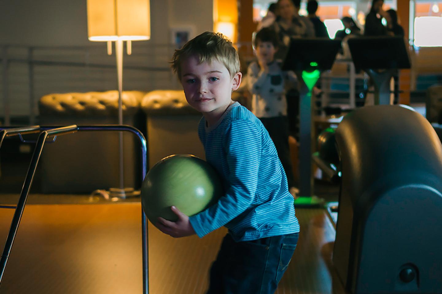 Young boy in blue shirt holding green bowling ball indoors.