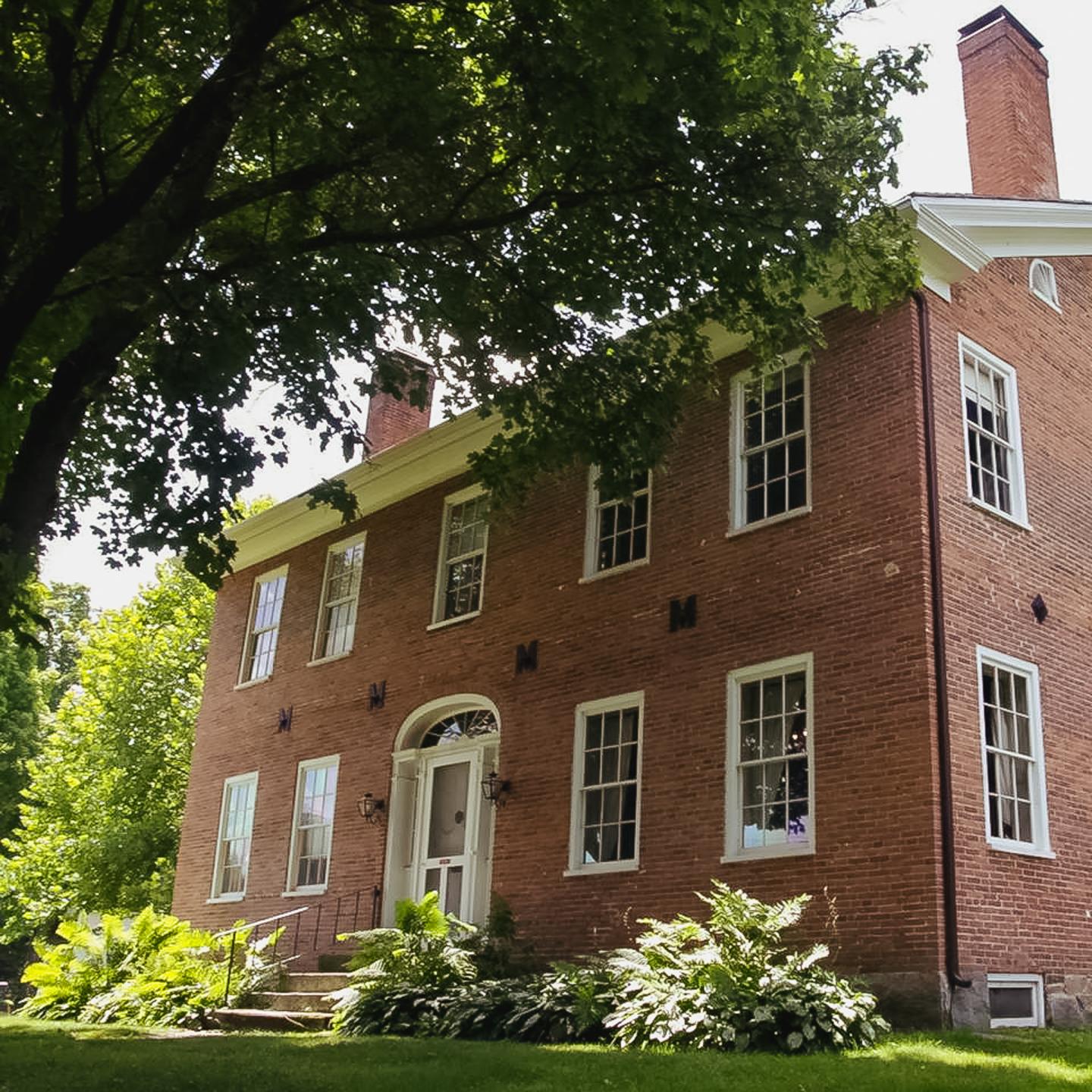 Red brick house with white trim, surrounded by green trees and shrubs.
