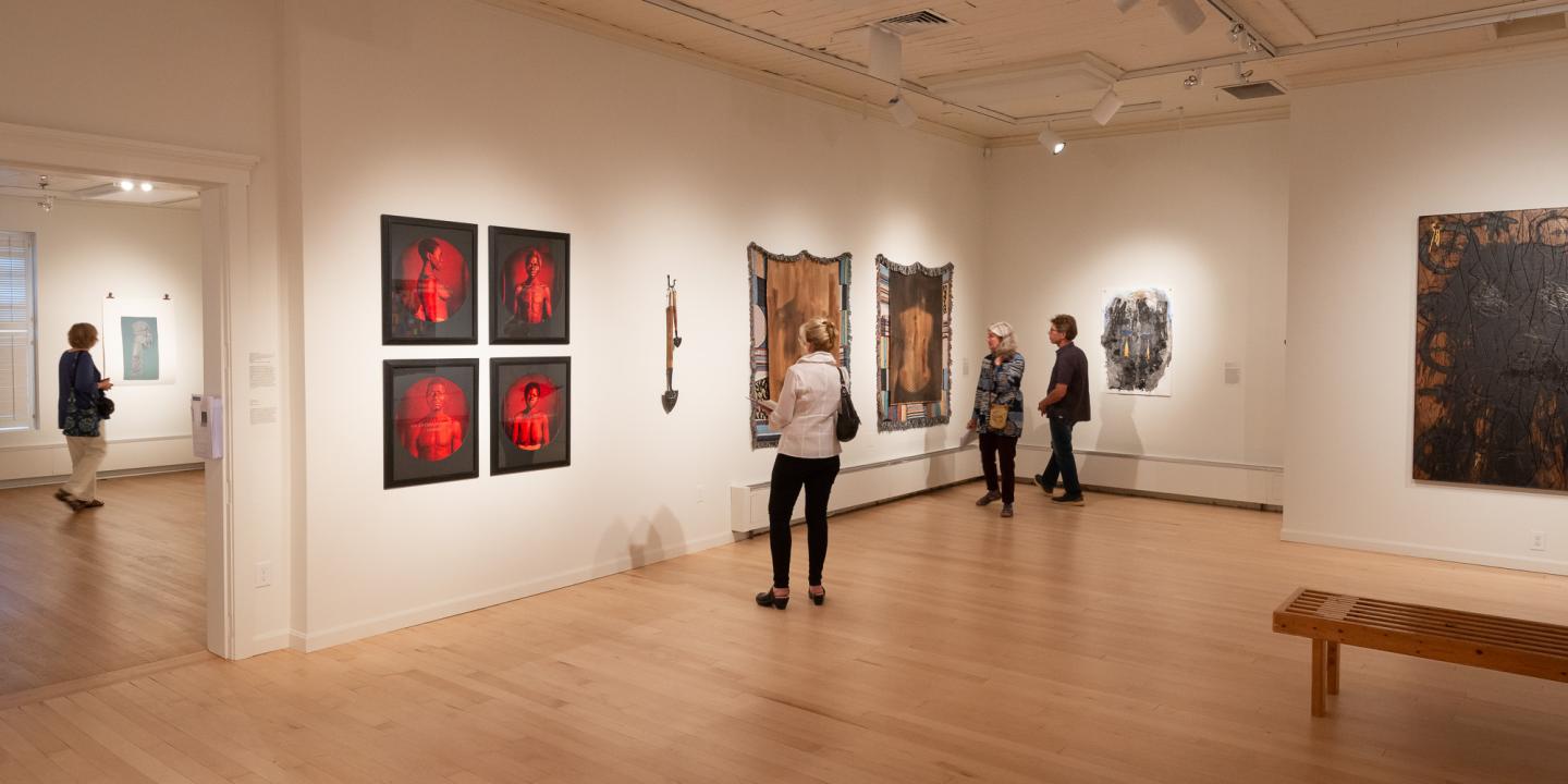 Art gallery with people viewing paintings on white walls.