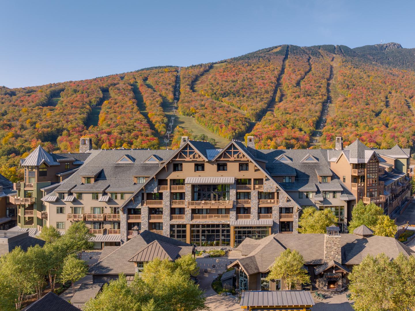 Mountain resort hotel with colorful autumn foliage in the background.